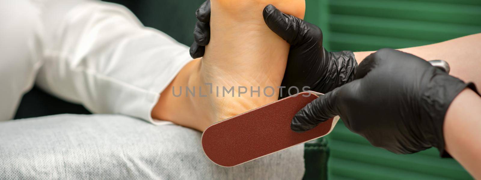 Peeling of Heels. Hands of pedicure master scrape dead from heel skin by special grater in spa salon. by okskukuruza