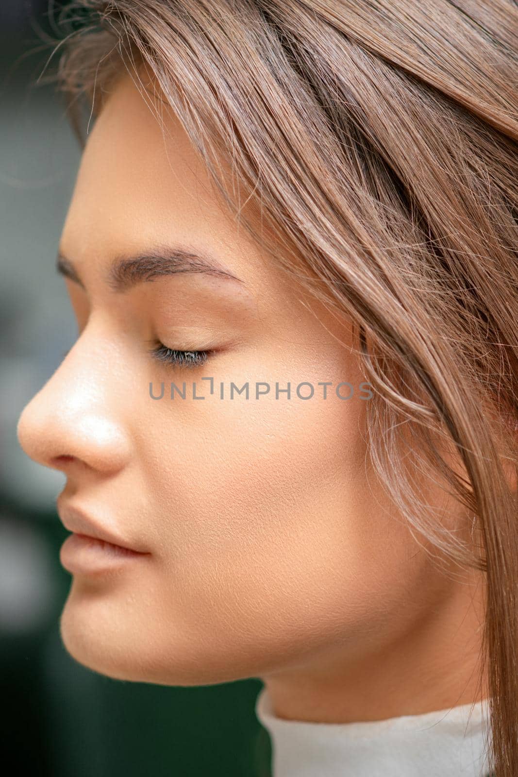 Portrait of a sensual young caucasian woman with closed eyes showing makeup tan on her face and hairstyle in a beauty salon. by okskukuruza