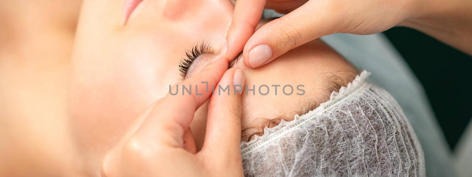 Manual sculpting face massage in the spa. Fingers of beautician make facial massage eyebrow of a young woman in cosmetology clinic, close up