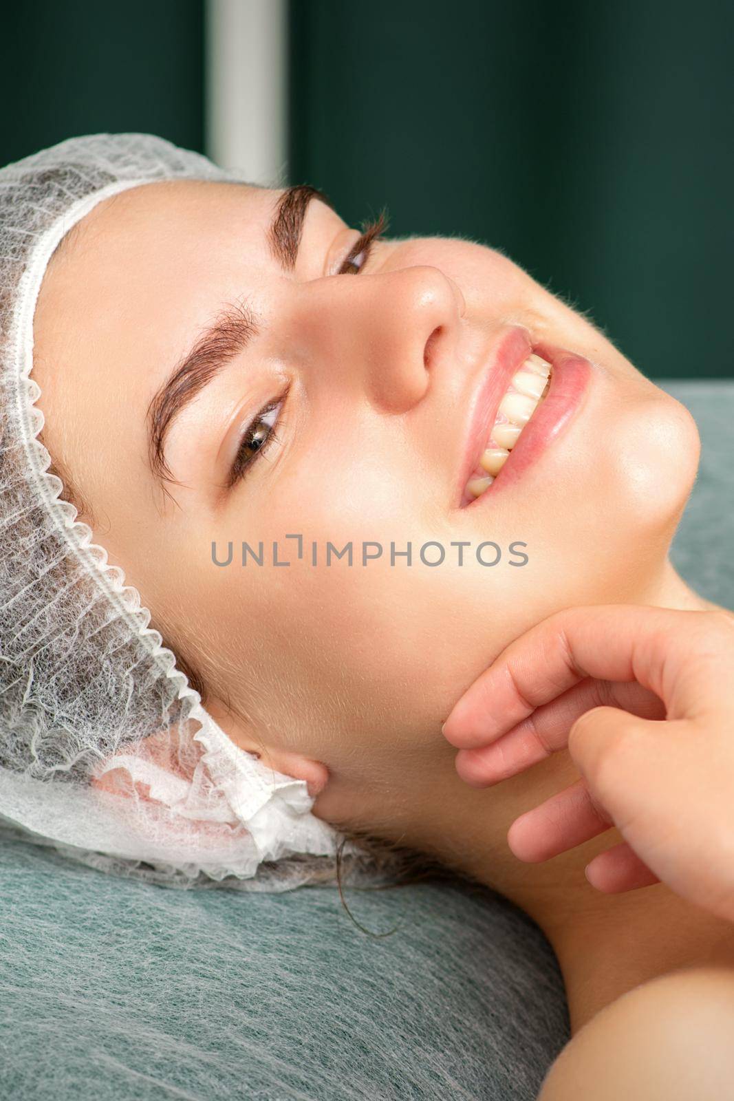 Plastic surgery and beauty concept. Hand of beautician examining and touching the face of beautiful young smiling caucasian woman