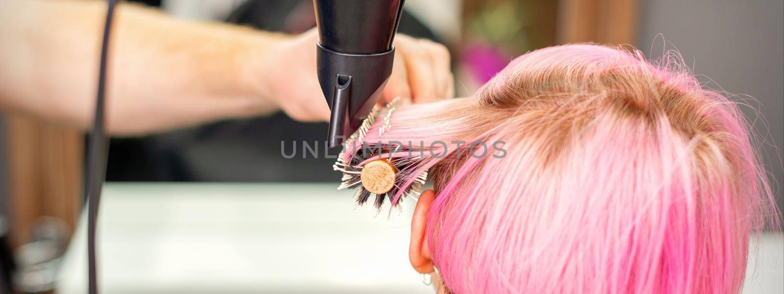 A professional hairdresser is drying long red hair with a hair dryer and round brush, close up