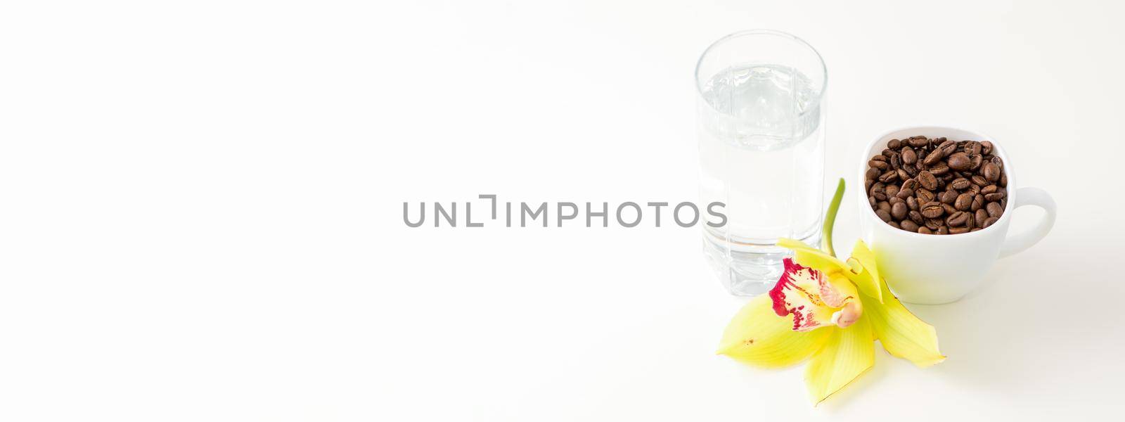 Cup of coffee beans and glass of water with yellow orchid flower against a white background