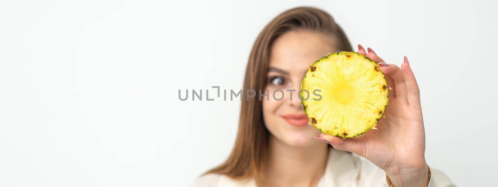 A young attractive pretty nice caucasian smiling woman holds ring slice pineapple covering her eye against a white background. Healthy eating concept. by okskukuruza