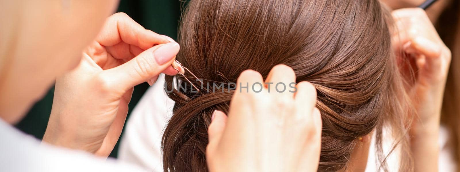 A hairdresser is making the hairstyle of a young brunette woman in a hair salon, close up