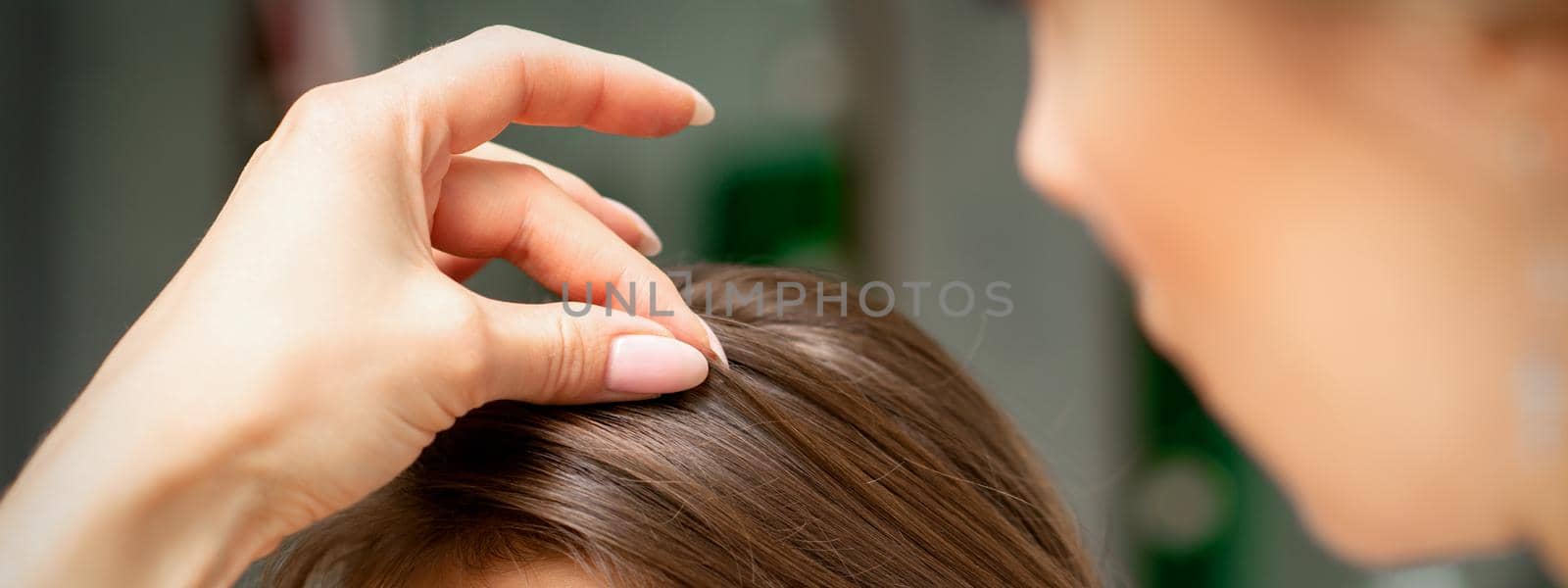 A hairdresser is making the hairstyle of a young brunette woman in a hair salon, close up. by okskukuruza