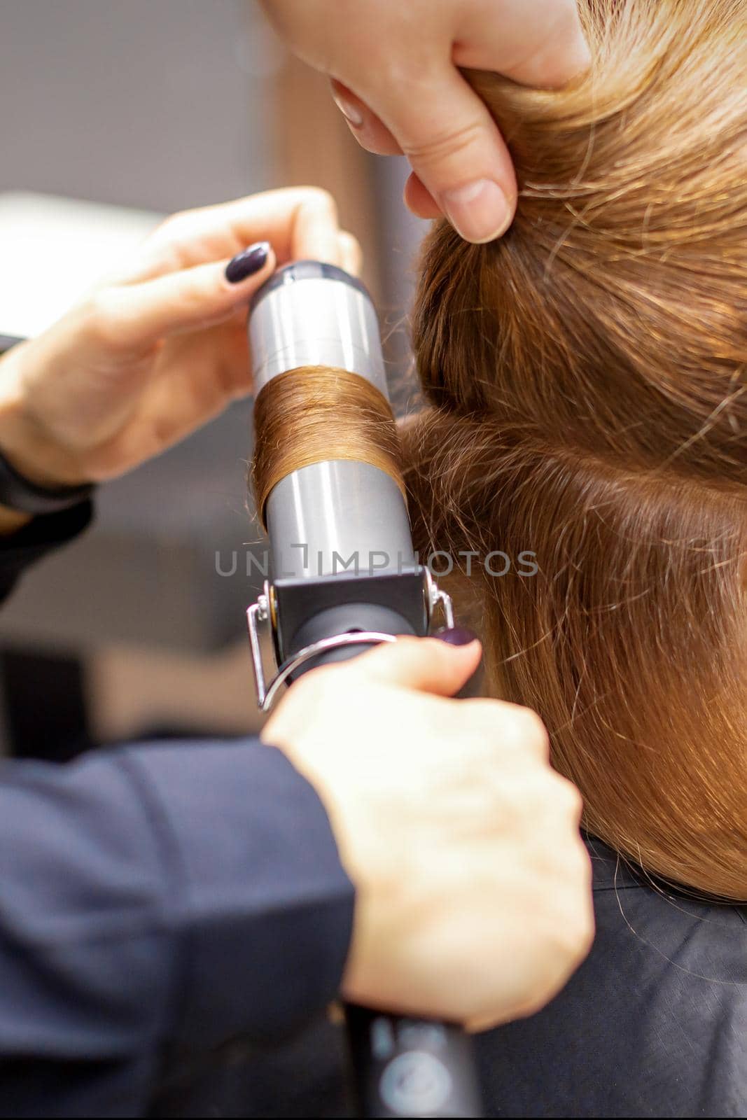 Hands of female hairstylist curls hair client with a curling iron in a hairdressing salon, close up. by okskukuruza