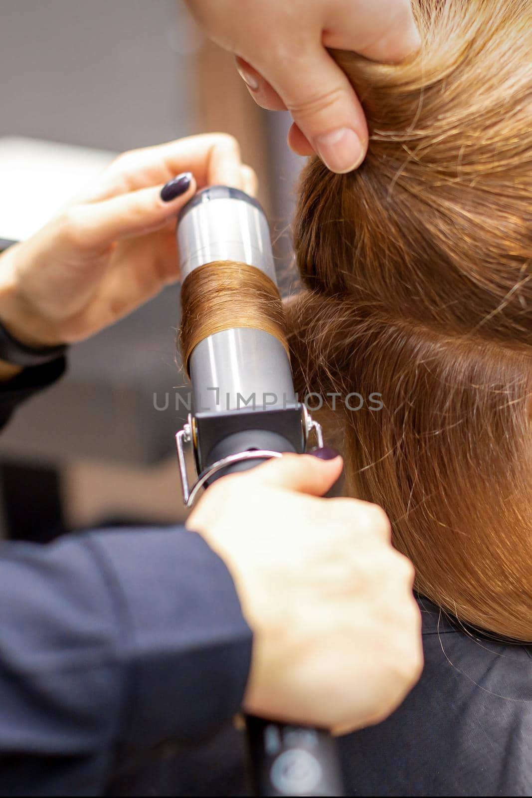 Hands of female hairstylist curls hair client with a curling iron in a hairdressing salon, close up