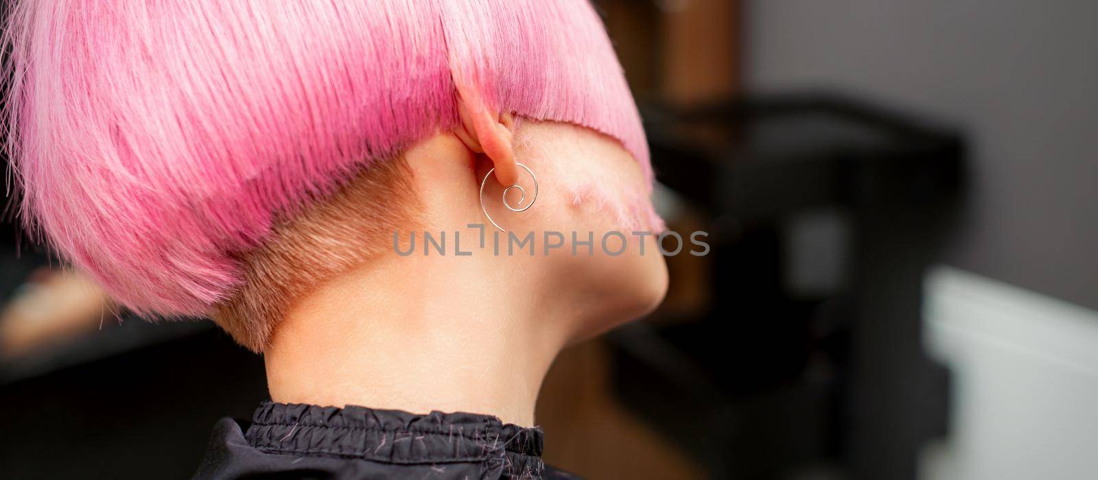 Styling and cutting dyed pink hair of young model back view in a hairdressing salon. Pink short hairstyle