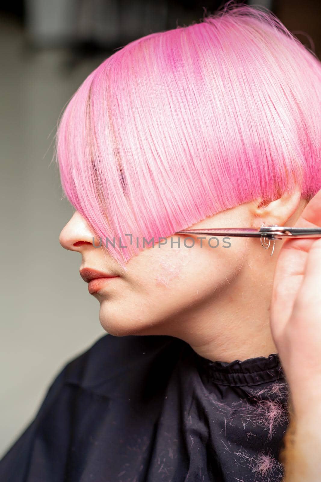 Hand of a hairdresser cutting short pink with scissor hair in a hairdressing salon, close up, side view