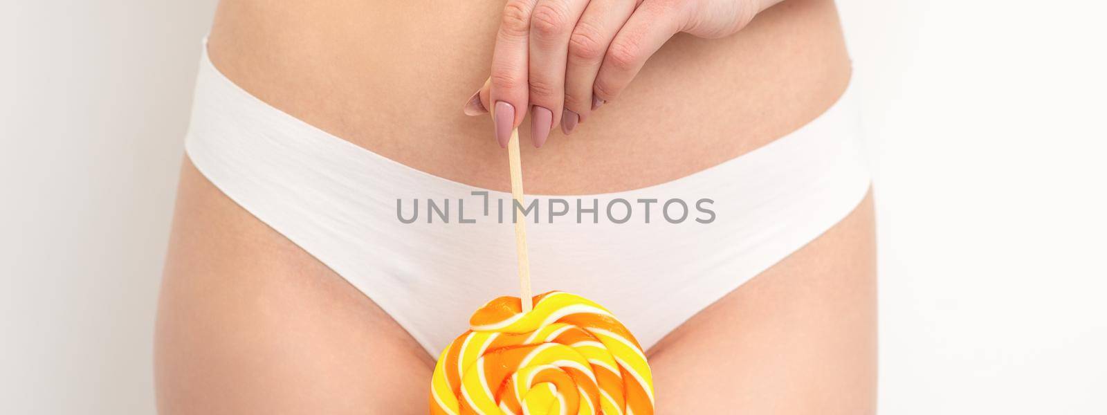 Hand of a woman wearing white panties holding lollipop on a stick covering the intimate area, the concept of intimate depilation, problems of intimate hygiene. by okskukuruza