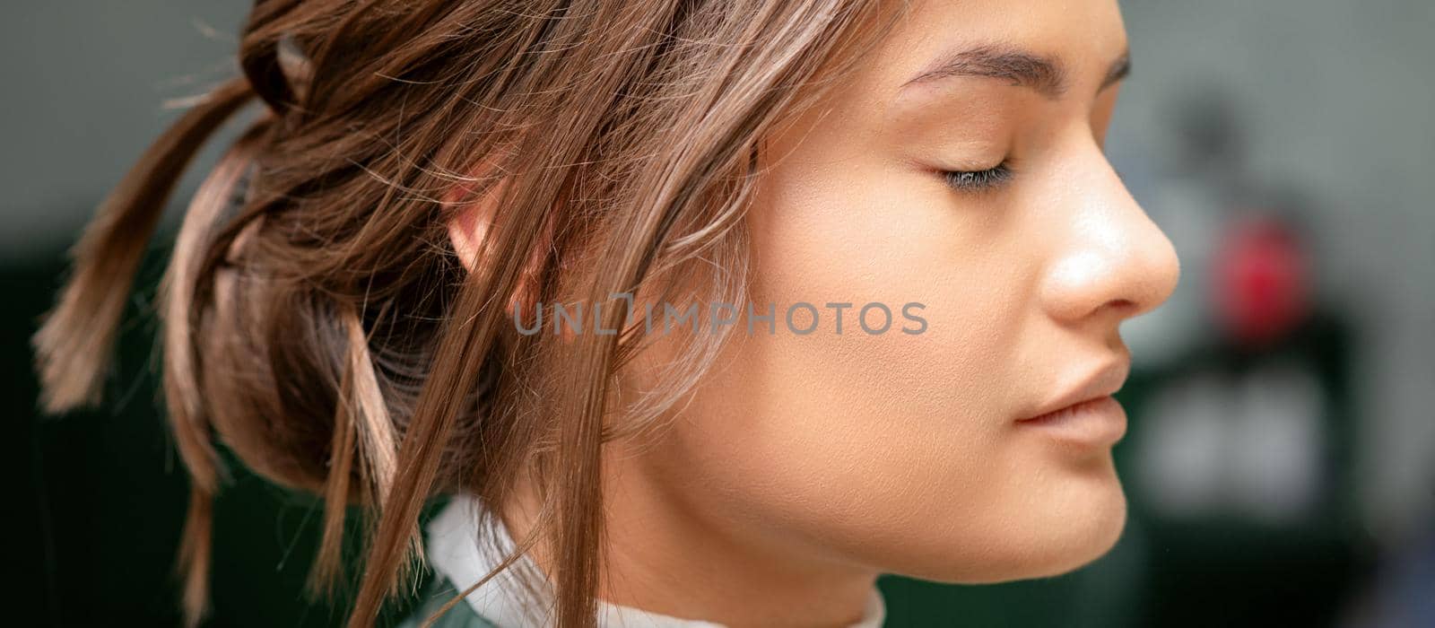 Portrait of a sensual young caucasian woman with closed eyes showing makeup tan on her face and hairstyle in a beauty salon. by okskukuruza