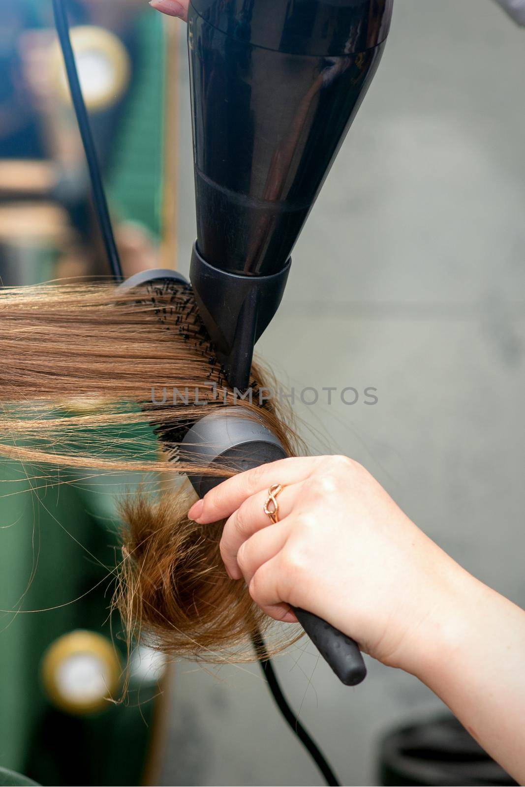 A hairdresser is drying long brown hair with a hairdryer and round brush in a hairdressing salon. by okskukuruza