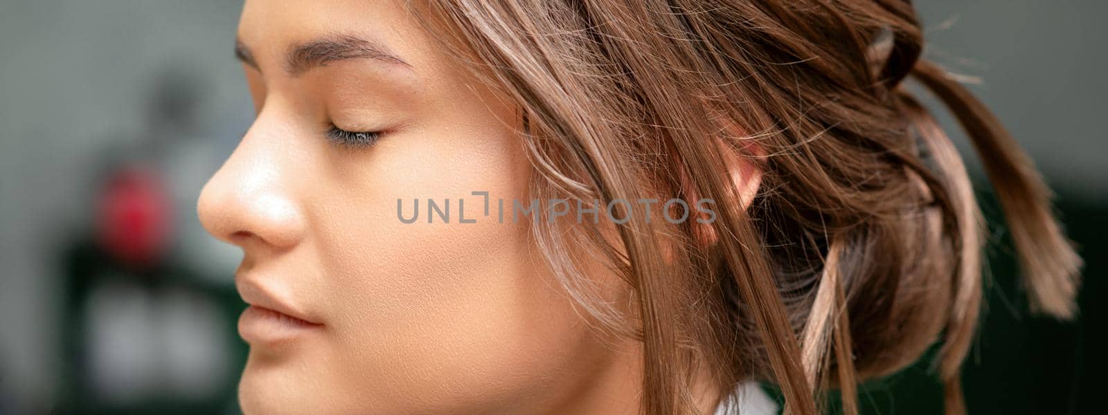 Portrait of a sensual young caucasian woman with closed eyes showing makeup tan on her face and hairstyle in a beauty salon
