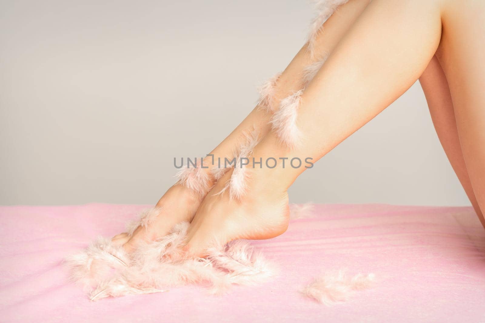 Hair removal and epilation concept. Beautiful long white smooth female legs with white feathers lying on the couch. by okskukuruza