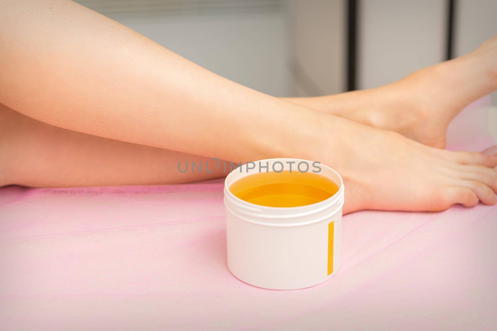 Woman legs with a white jar of wax sugaring before hair removal at the spa