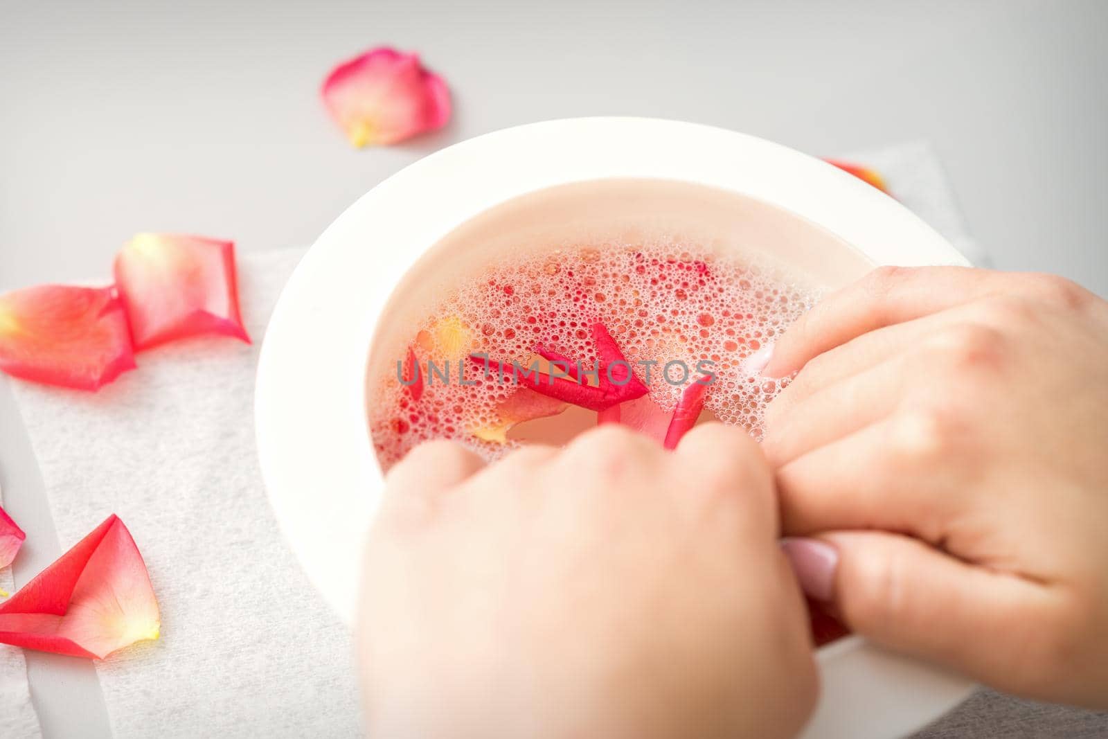 Female hands in a bowl of water with pink petals of rose flowers in spa. by okskukuruza