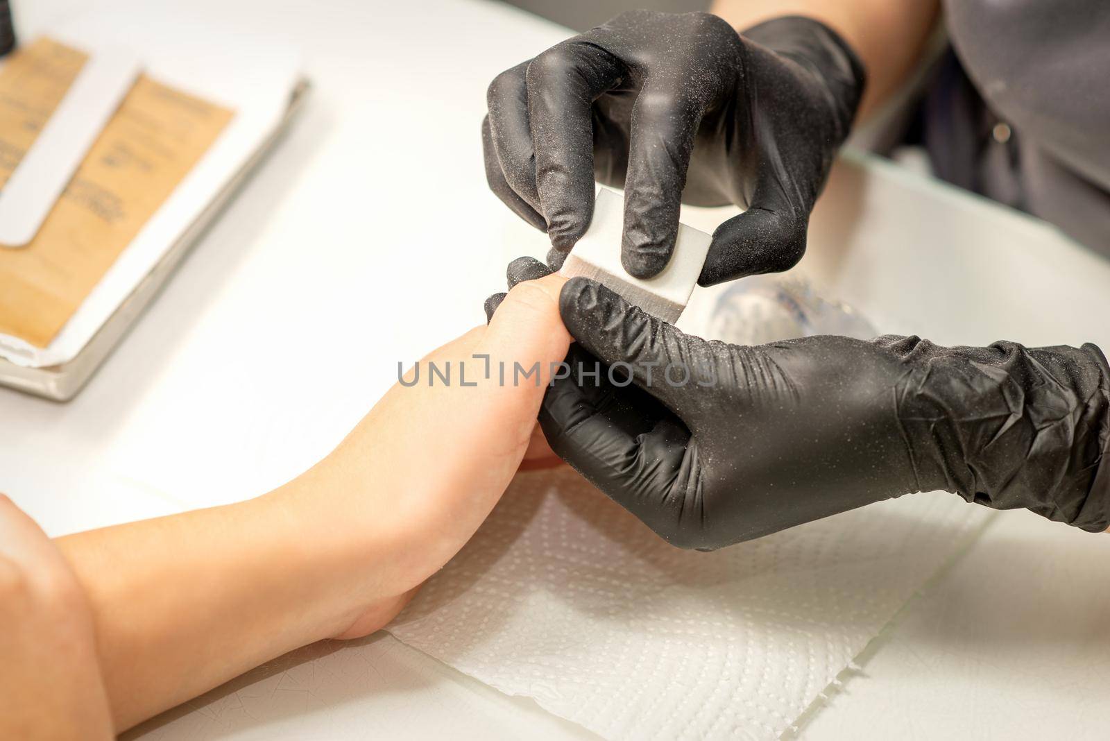 Close up of the caucasian hands of a professional manicurist are filing the nails of a young woman. Young caucasian woman receiving a manicure by a beautician with a nail file in a nail salon