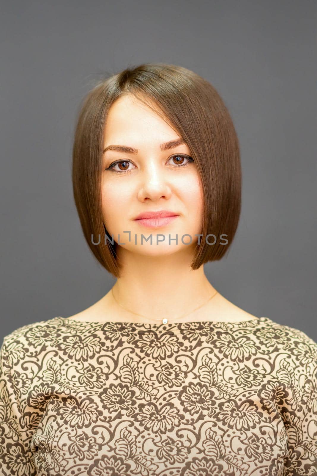 Beautiful young caucasian brunette woman with short hairstyle smiling and looking at camera against dark gray background with copy space. by okskukuruza