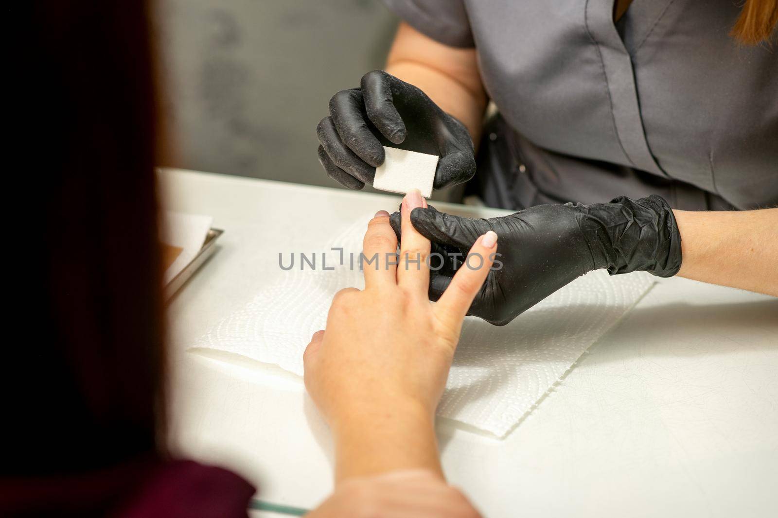 Close up of the caucasian hands of a professional manicurist are filing the nails of a young woman. Young caucasian woman receiving a manicure by a beautician with a nail file in a nail salon. by okskukuruza