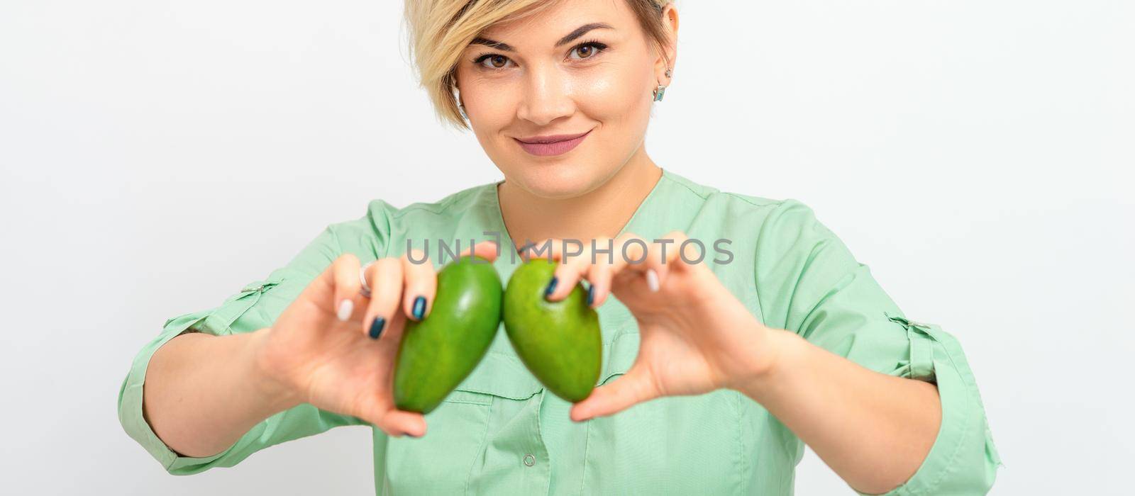 Female nutritionist doctor wearing green workwear holding green organic avocado fruit. Healthy lifestyle concept