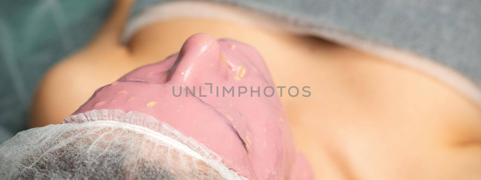 Women skin beauty treatment care. Young woman with alginate cosmetic pink mask on facial skin in beauty spa salon. by okskukuruza