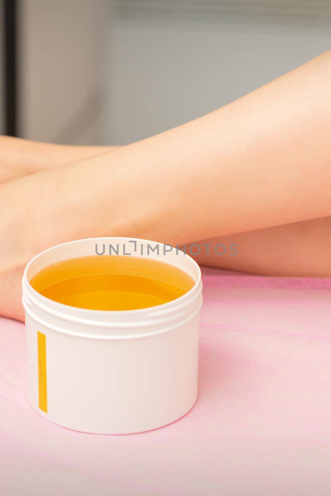 Woman legs with a white jar of wax sugaring before hair removal at the spa