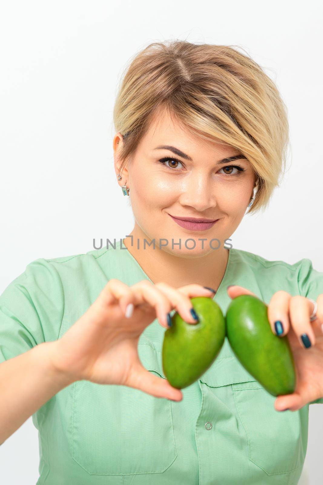 Female nutritionist doctor wearing green workwear holding green organic avocado fruit. Healthy lifestyle concept. by okskukuruza