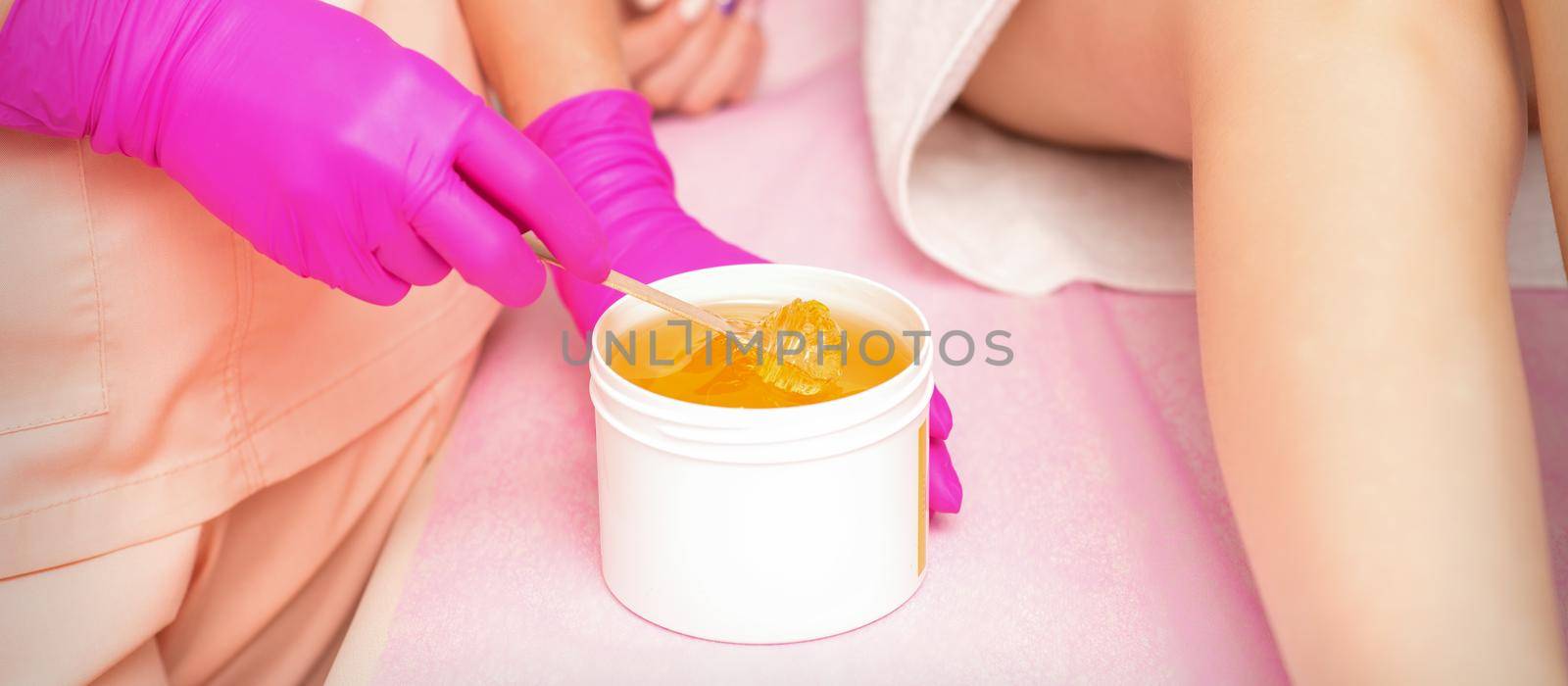 Beautician with a white jar of wax sugaring before hair removal at the spa