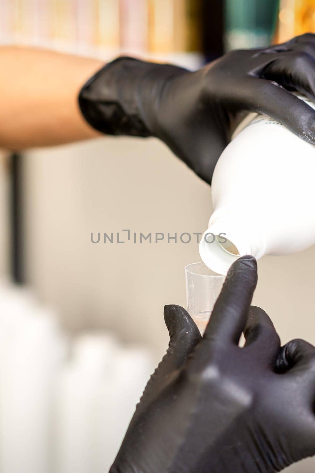 A hairdresser in black gloves is preparing hair dye with a bottle in a hair salon, close up