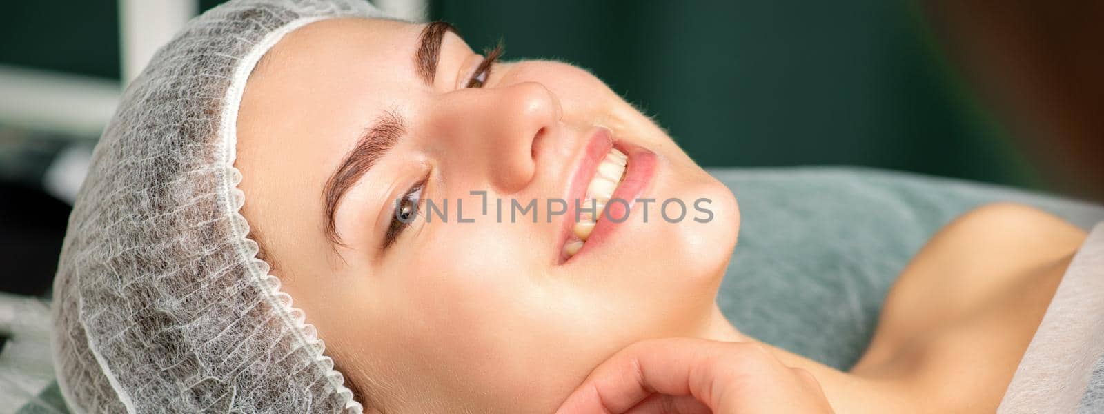 Plastic surgery and beauty concept. Hand of beautician examining and touching the face of beautiful young smiling caucasian woman. by okskukuruza