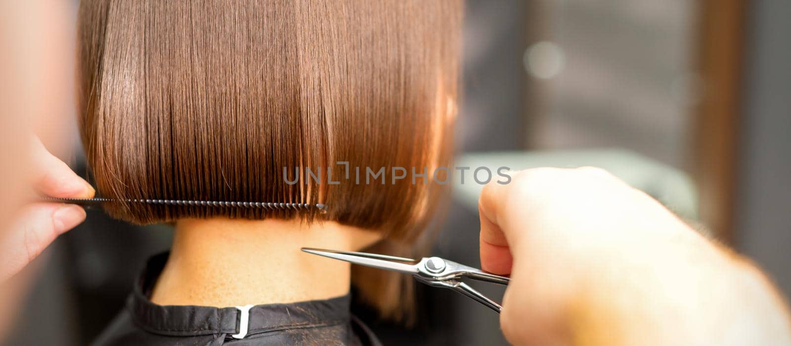 Haircut of short hair of young white woman by hands of a hairdresser in a hair salon, back view, close up. by okskukuruza