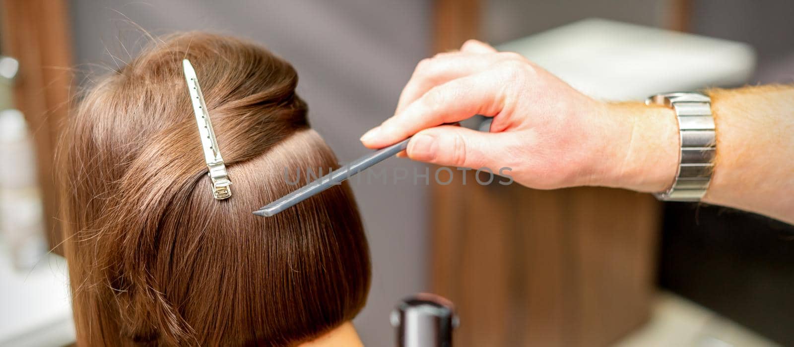 A hairdresser is combing the short hair of the brunette female client in the hairdresser salon, back view. by okskukuruza