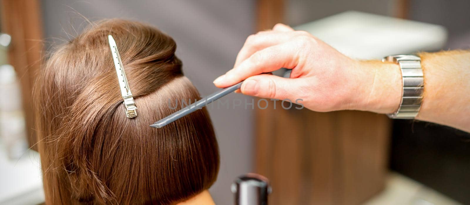 A hairdresser is combing the short hair of the brunette female client in the hairdresser salon, back view