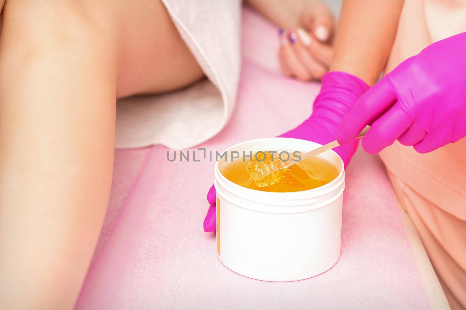 Beautician with a white jar of wax sugaring before hair removal at the spa