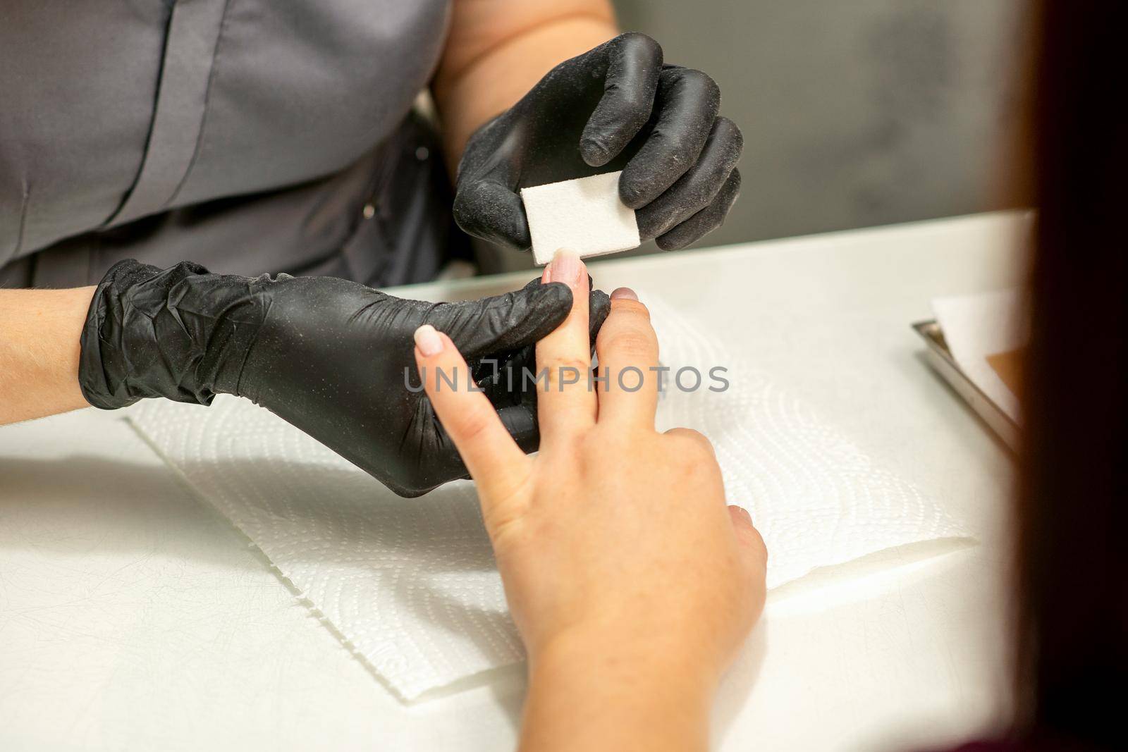 Close up of the caucasian hands of a professional manicurist are filing the nails of a young woman. Young caucasian woman receiving a manicure by a beautician with a nail file in a nail salon. by okskukuruza