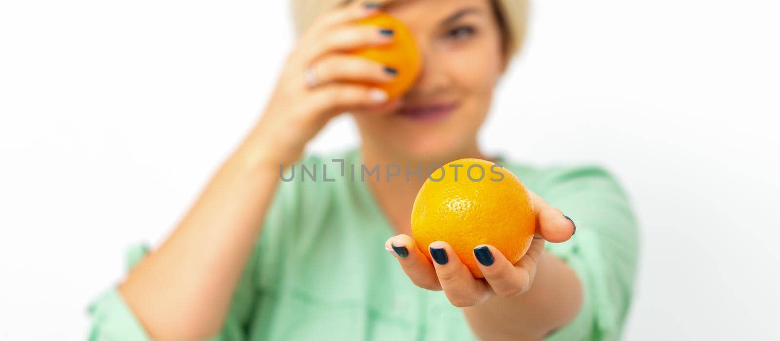 Smiling female nutritionist holding a whole orange, offering and looking at camera over white background, healthy diet concept