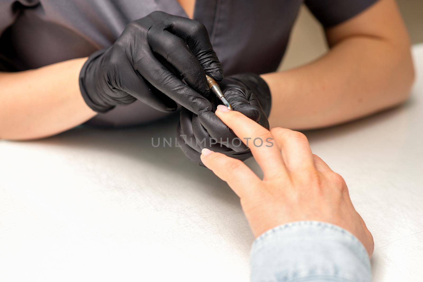 Close up professional manicurist master holding customer hand while using a cuticle pusher in a nail salon