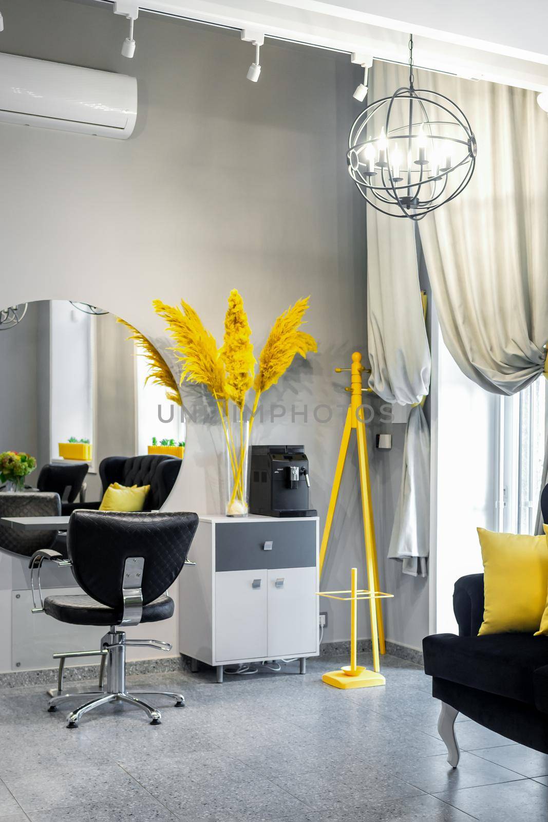 Modern small bright hair and beauty salon in black and yellow colors with gray walls and floor and black sofa with yellow cushions