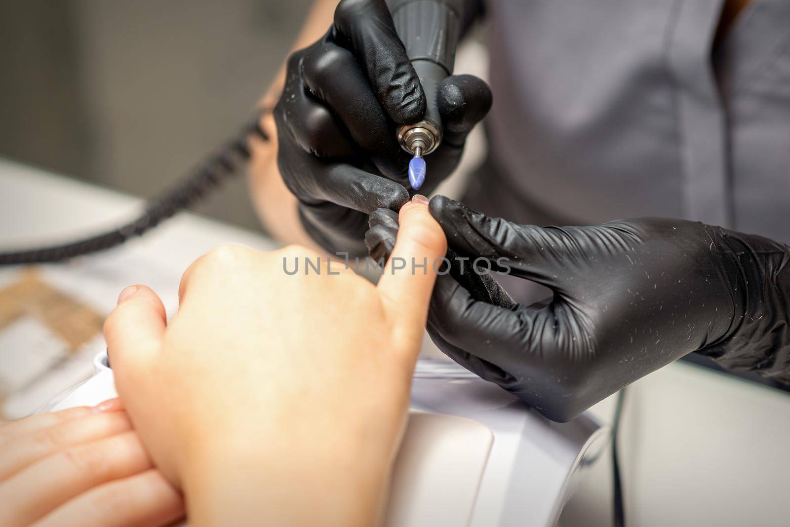 Manicure master uses electric nail file machine in a nail salon, close up