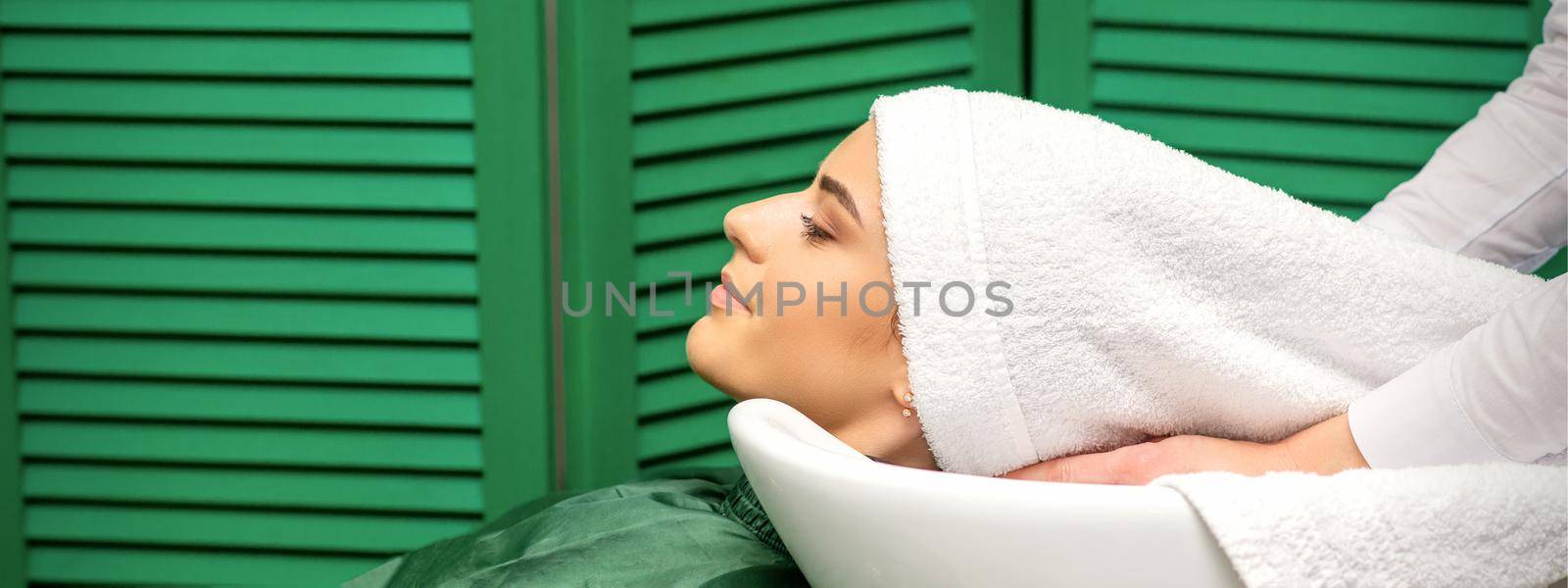 Hairdresser wraps hair of a young caucasian woman in a white towel after washing head in the hairdressing salon