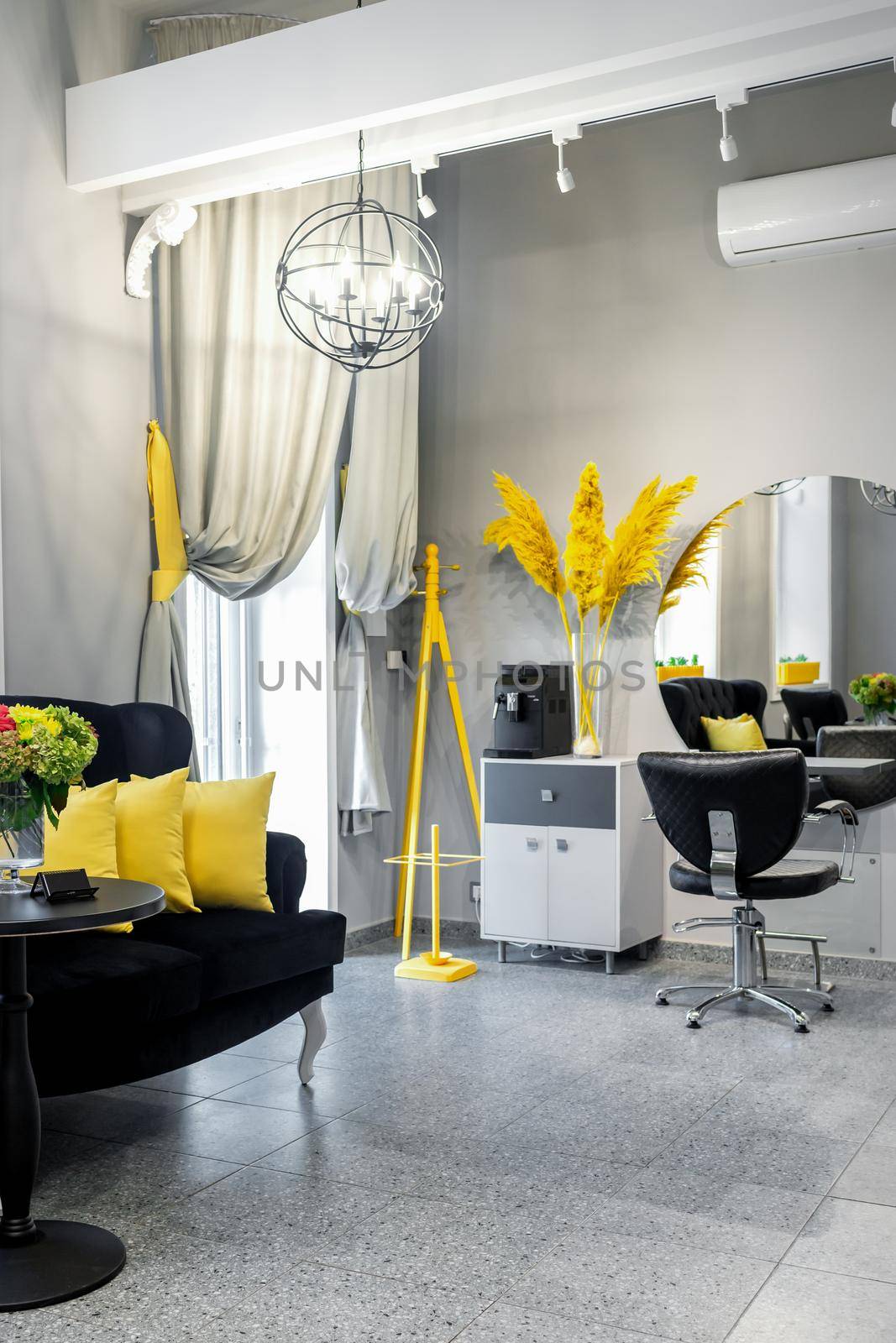 Modern small bright hair and beauty salon in black and yellow colors with gray walls and floor and black sofa with yellow cushions