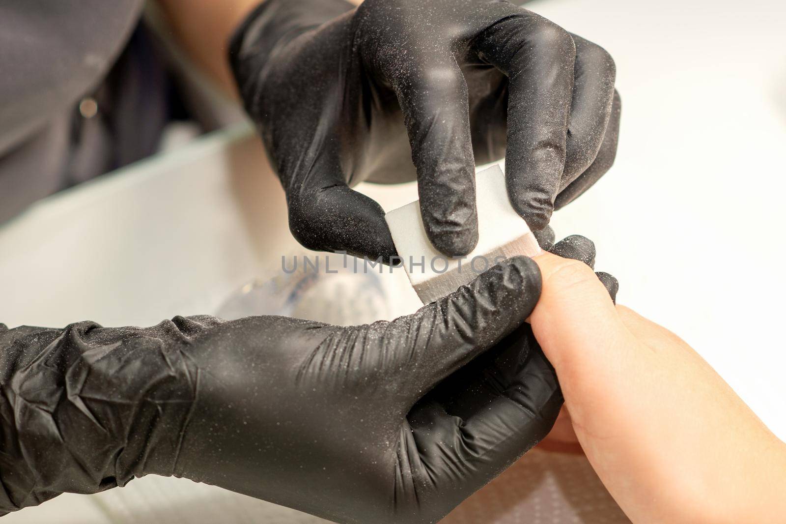 Close up of the caucasian hands of a professional manicurist are filing the nails of a young woman. Young caucasian woman receiving a manicure by a beautician with a nail file in a nail salon. by okskukuruza