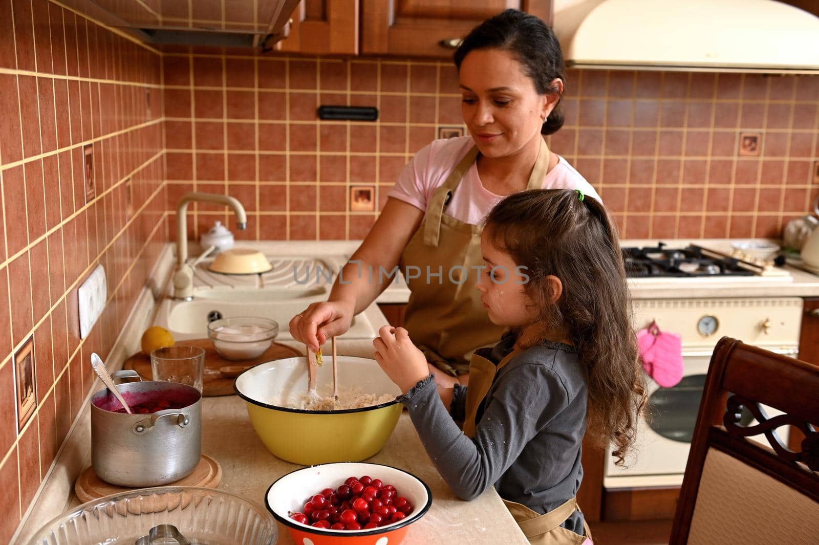 Happy multi-ethnic family, a loving mother and daughter baking together, kneading dough in the home kitchen by artgf
