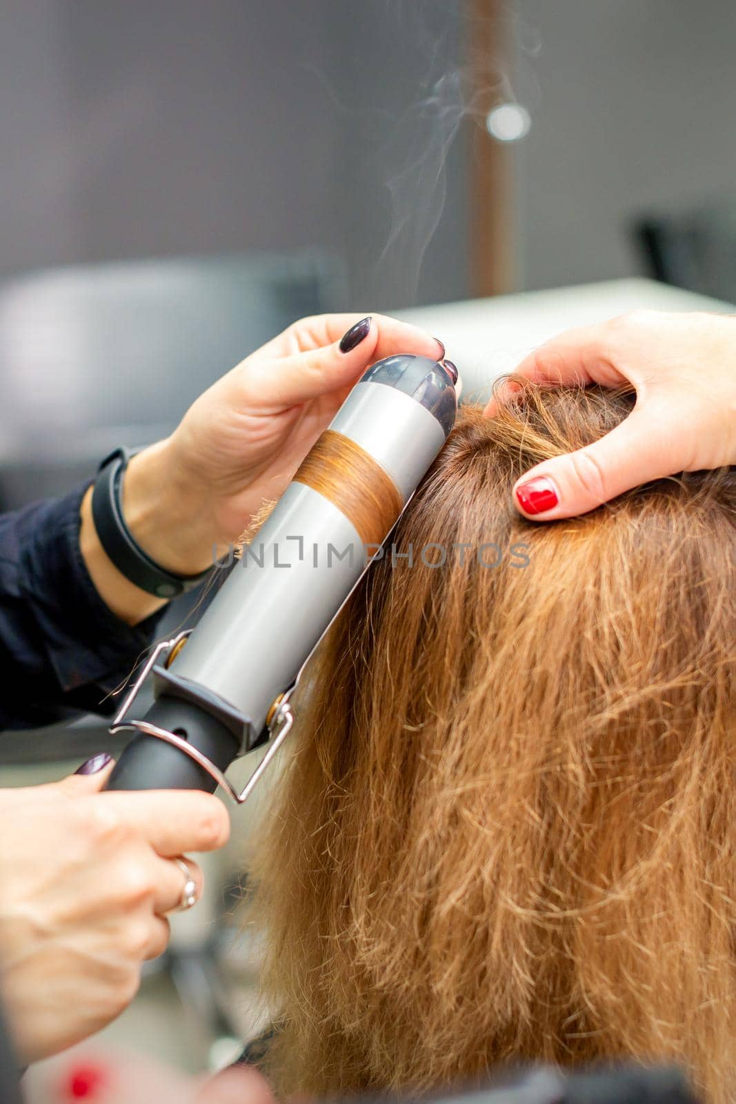 Hands of female hairstylist curls hair client with a curling iron in a hairdressing salon, close up. by okskukuruza