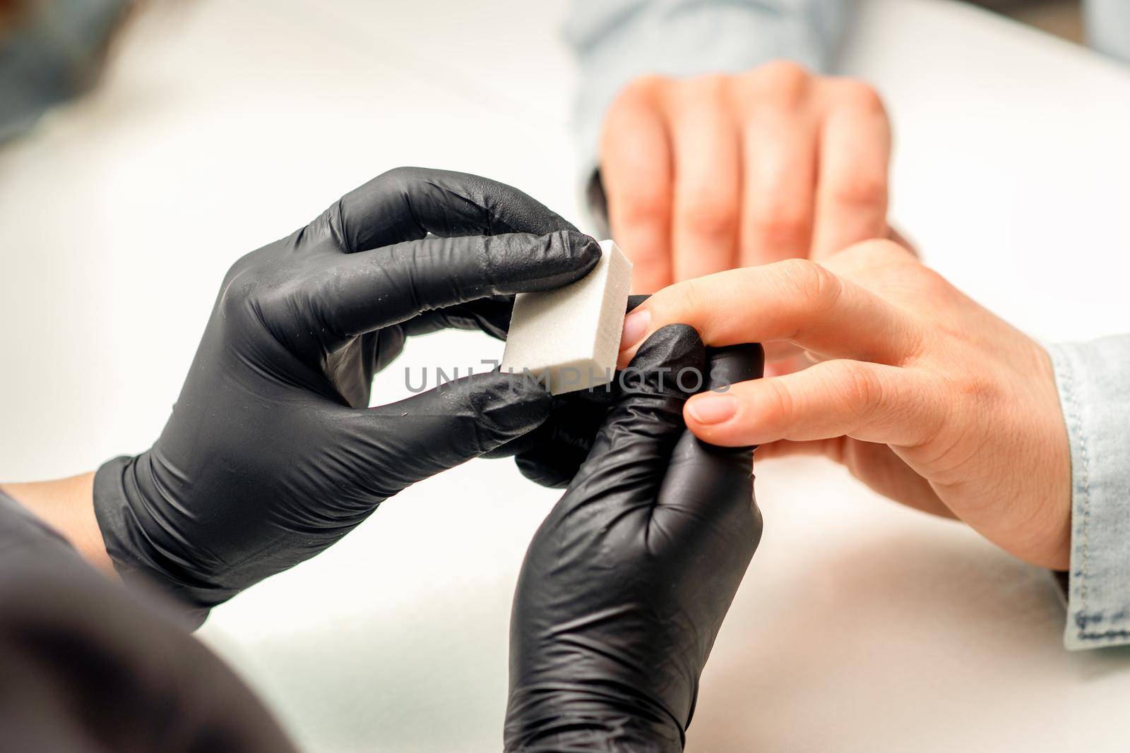 Close up of the caucasian hands of a professional manicurist are filing the nails of a young woman. Young caucasian woman receiving a manicure by a beautician with a nail file in a nail salon. by okskukuruza