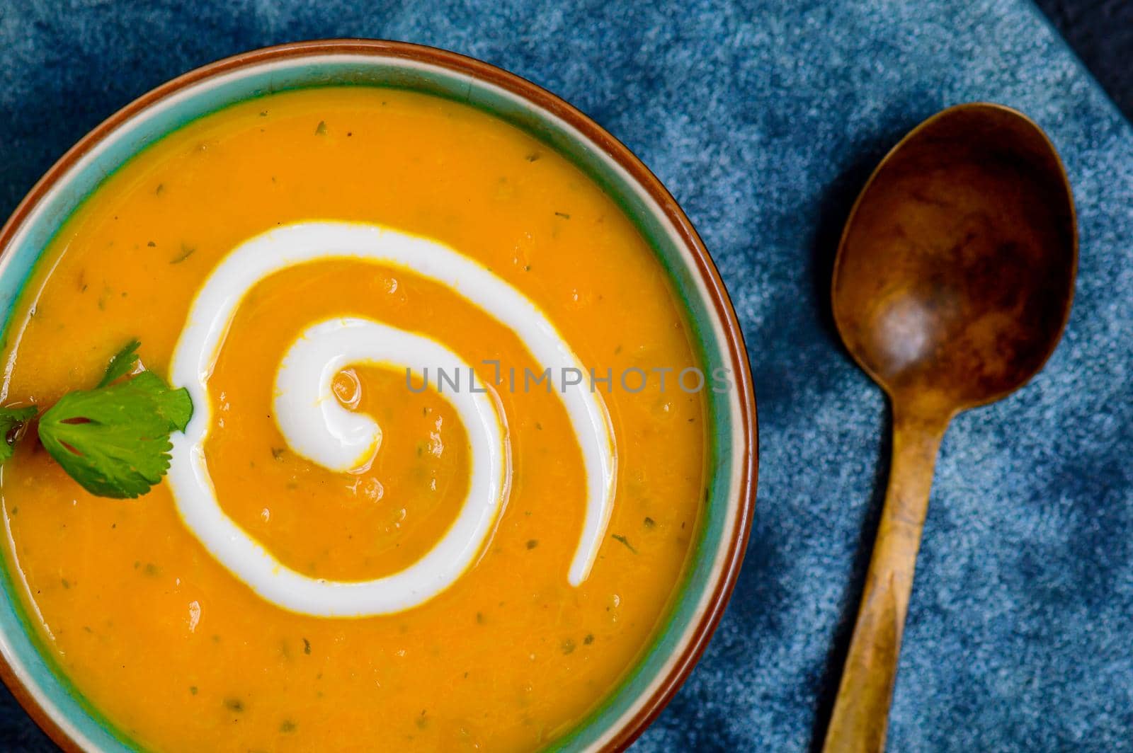 Autumnal spiced carrot and coriander soup with a swirl of cream on blue and black tabletop