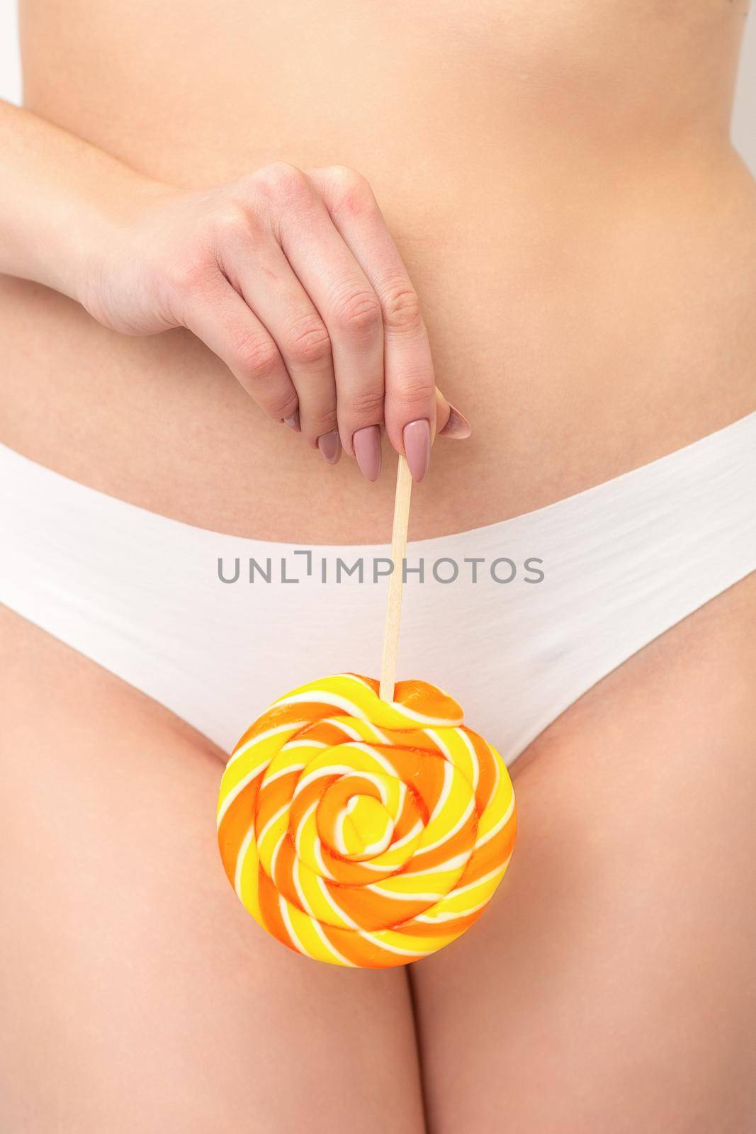 Hand of a woman wearing white panties holding lollipop on a stick covering the intimate area, the concept of intimate depilation, problems of intimate hygiene