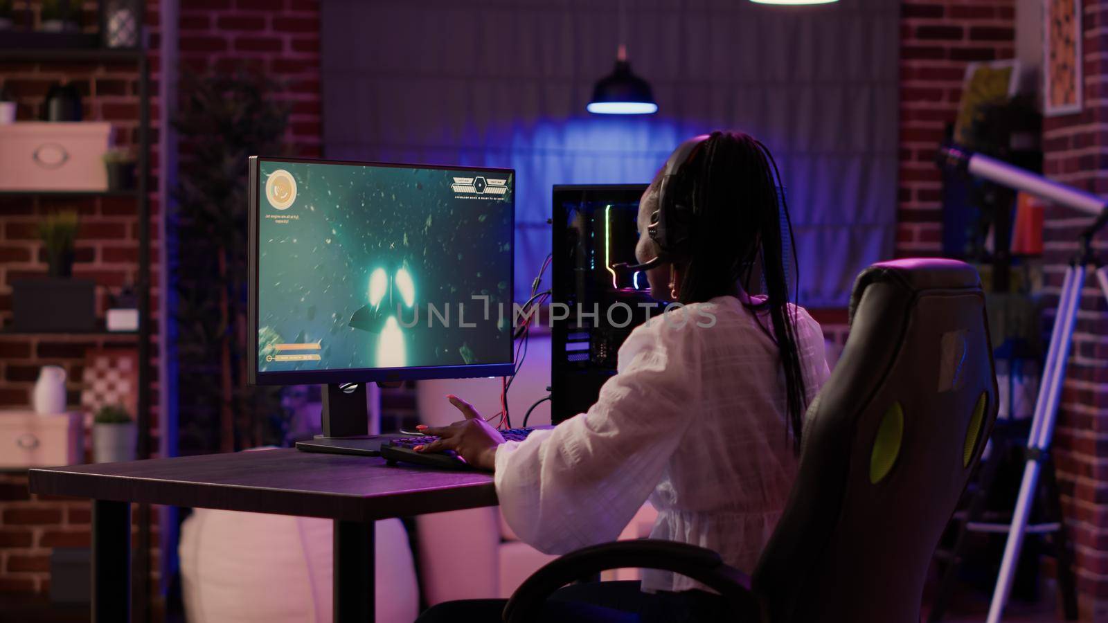 Woman playing multiplayer space shooter simulation enjoying free time using pc gaming setup by DCStudio