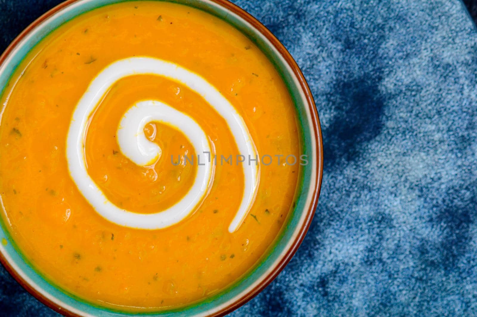 Autumnal spiced carrot and coriander soup with a swirl of cream on blue and black tabletop