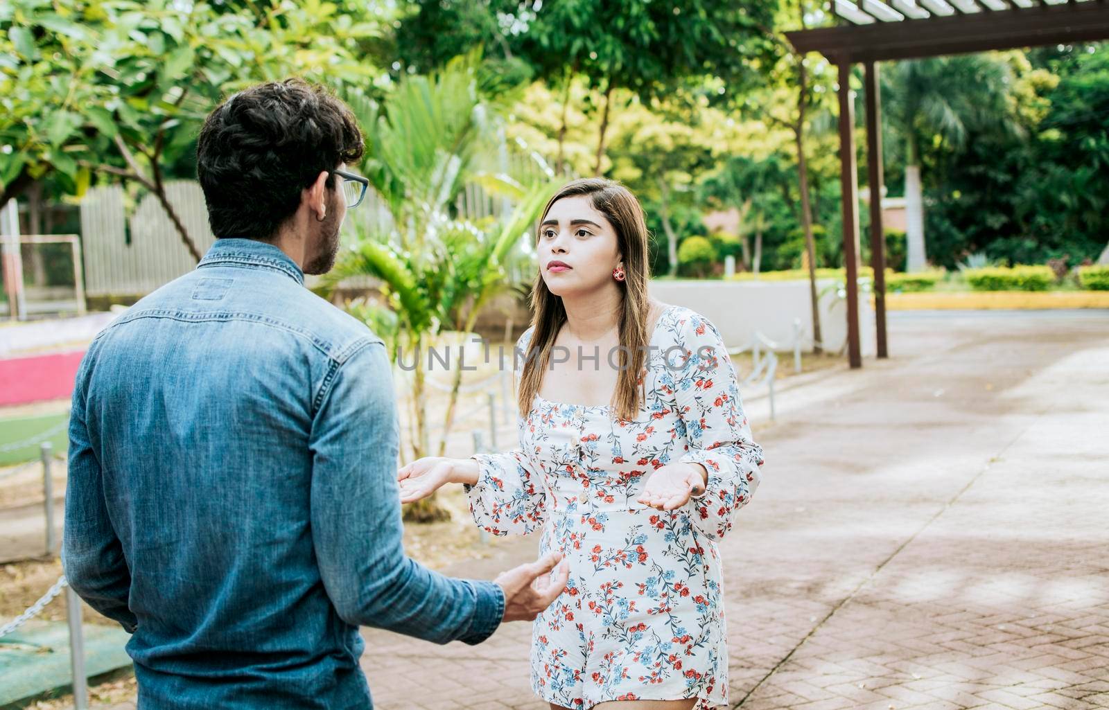 Unhappy couple standing arguing in a park. Disgusted teenage couple arguing in a park, Man and woman arguing in a park. Young couple arguing misunderstanding in a park